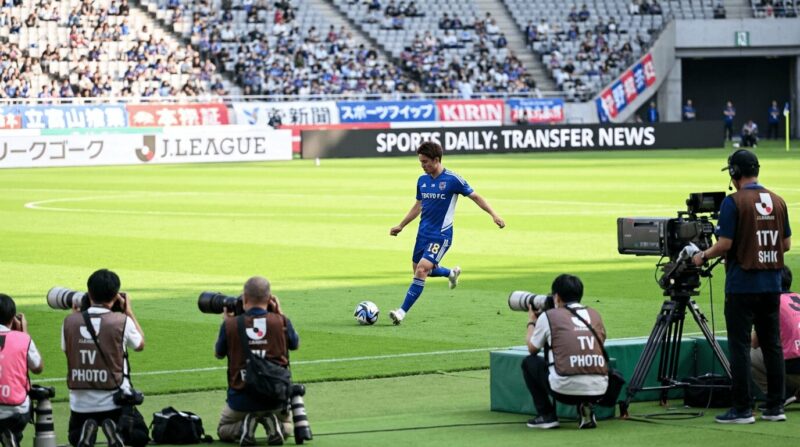 ピッチ上でプレーする選手とカメラマンの画像