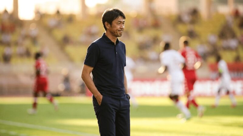 試合をする選手たちをサイドラインで見つめて思索する監督の姿